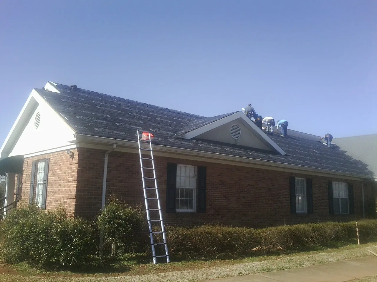Crew tearing shingles off a brick ranch roof with a ladder set — Metal Roof Repair work by our crew in New Wilmington