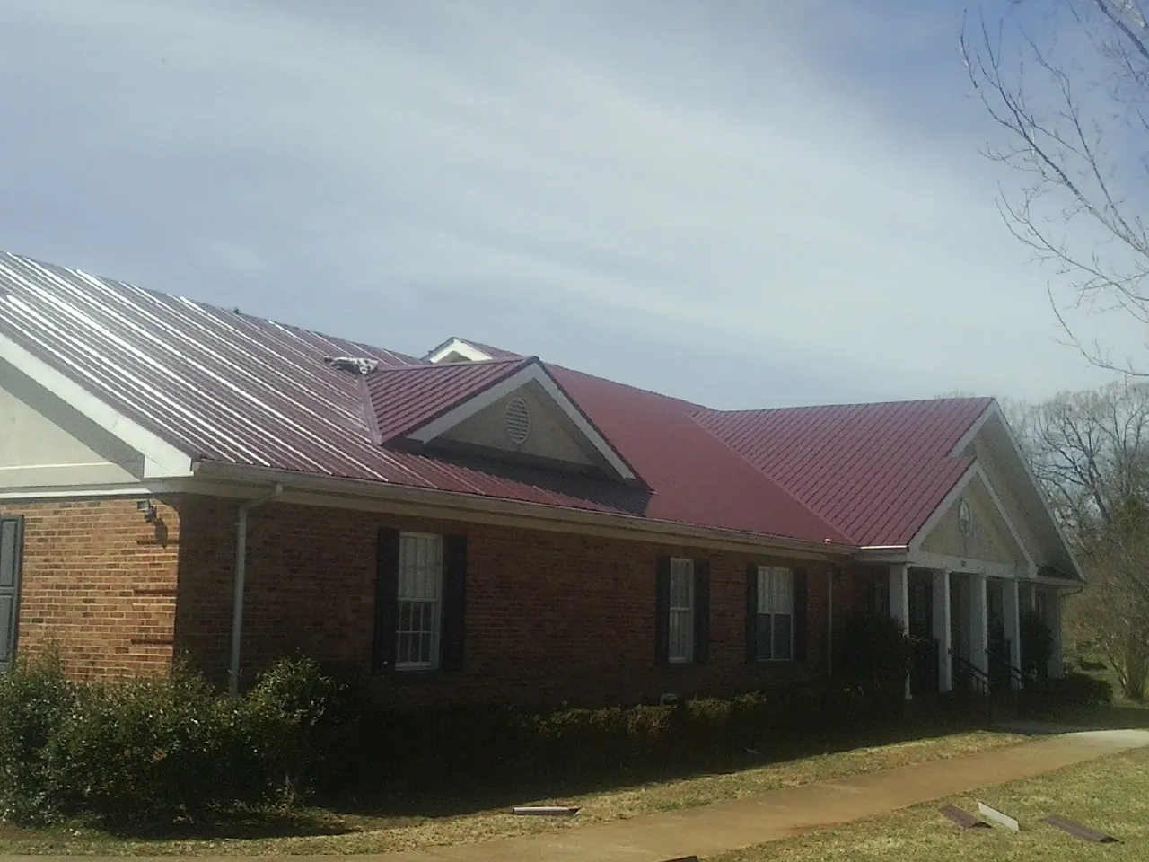 Red metal roof with gabled entries on a long brick building, from a Hail Damage Roof Repair job in New Wilmington