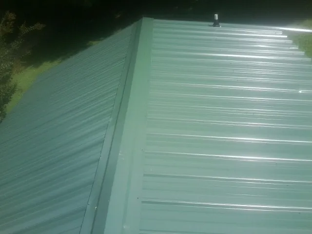 New green metal panels meeting at the ridge of a roof — Flat Roof Repair work by our crew in New Wilmington