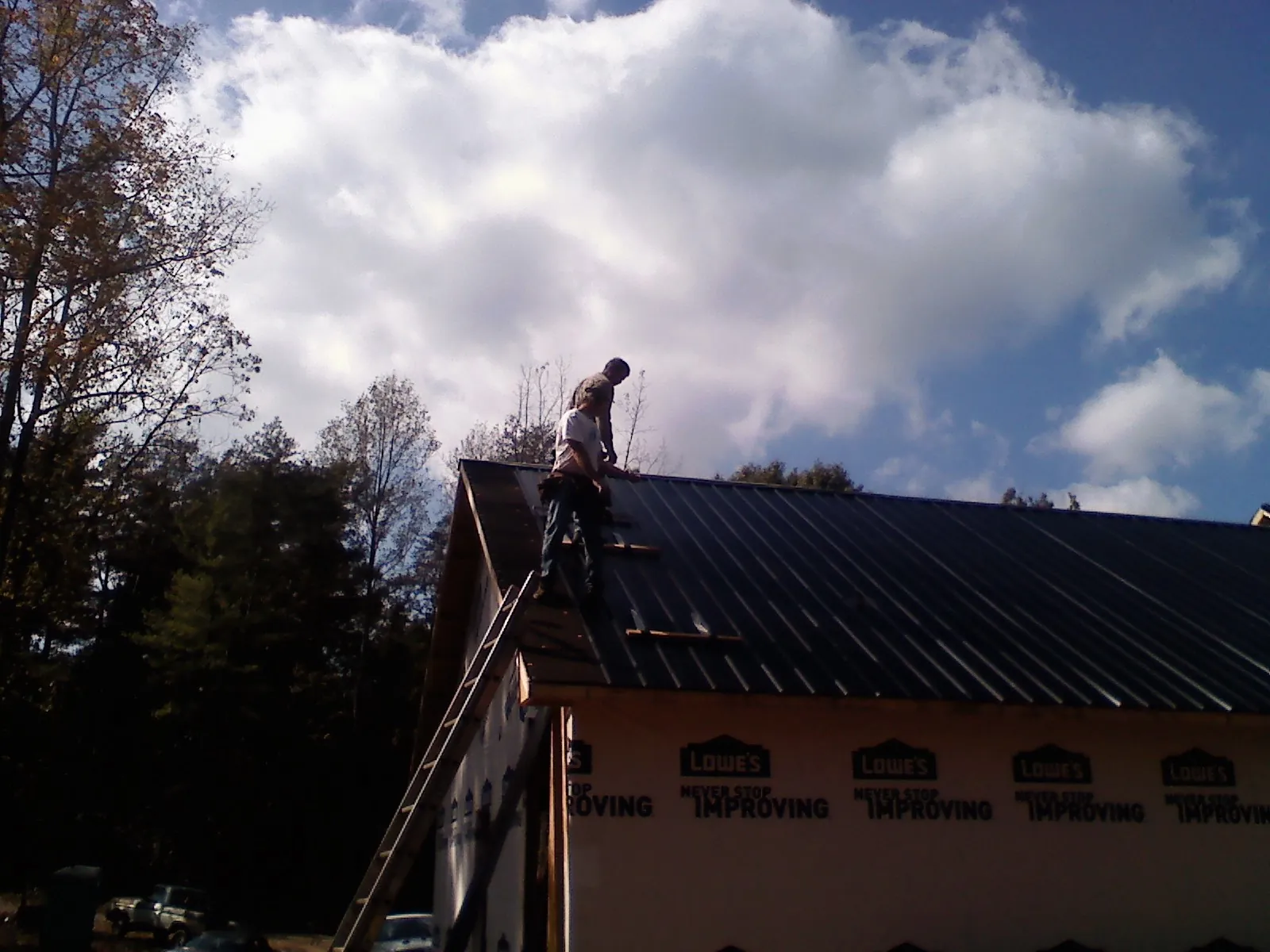 Roofer fastening dark metal panels high against a cloudy sky, from a Roof Inspection job in New Wilmington