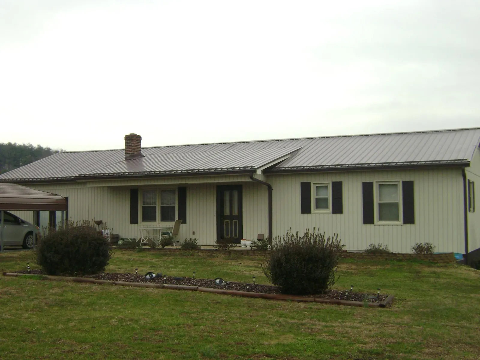Brown metal roof on a cream sided ranch home with a brick chimney in New Wilmington