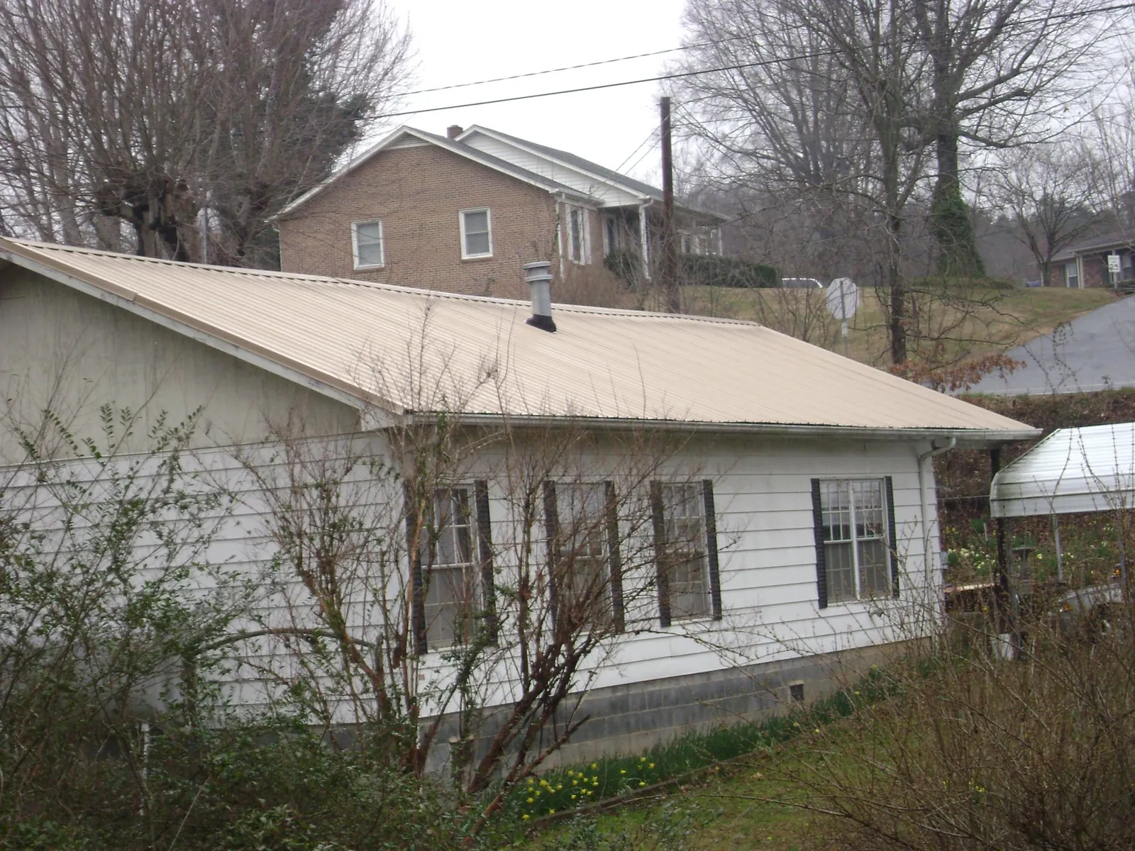 Tan metal roof on a white sided house set into a hillside — Commercial Roofing by Roofing Brothers in New Wilmington